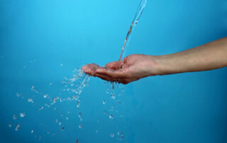 Adult woman holding a palm under water spout over blue background, ecology and water problem, healthy lifestyle, food and drink concept, studio shot